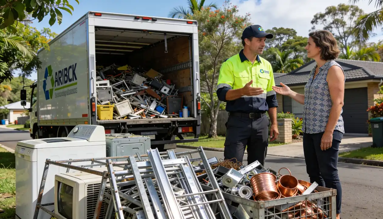 A recycling service professional in a hi-vis vest discussing responsible scrap disposal with a female homeowner beside a large collection of scrap metal copper pipes and old appliances in front of an open recycling truck on a Queensland suburban street.